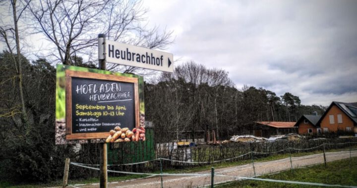 Hinweisschild des Hofladen Heubrachhof in Kleinostheim, der Bauernhof im Hintergrund.